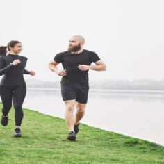 Couple jogging and running outdoors in park near the water. Young bearded man and woman exercising together in morning