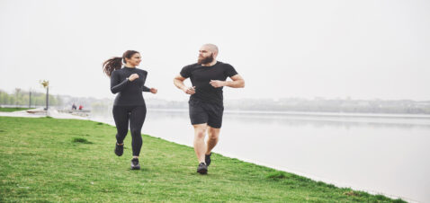Couple jogging and running outdoors in park near the water. Young bearded man and woman exercising together in morning