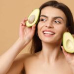 close-up-brunette-half-naked-woman-with-perfect-skin-nude-make-up-holds-avocado-isolated-beige-pastel-wall