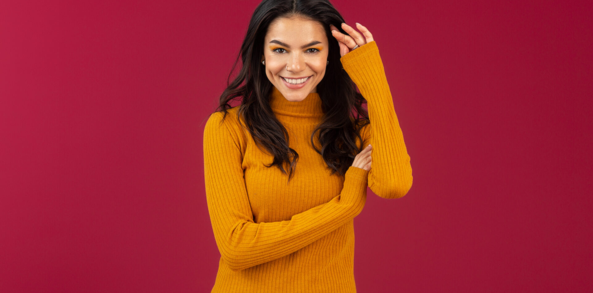 portrait of pretty smiling stylish brunette hispanic woman in yellow autumn winter fashion dress sweater posing isolated on red studio background